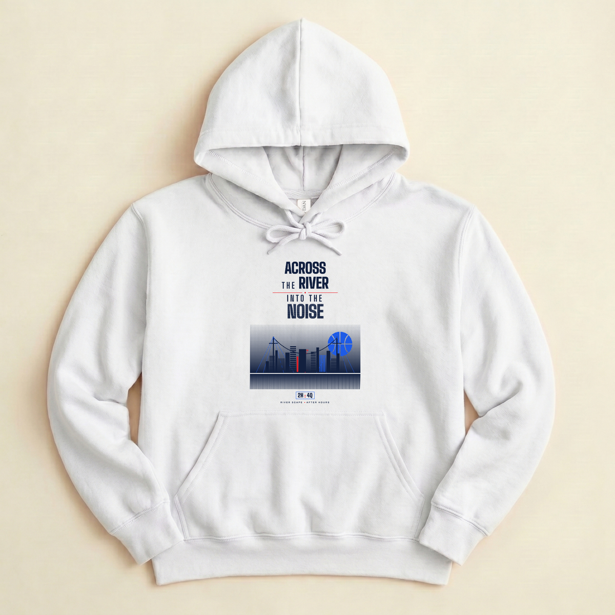A white pullover hoodie laid flat on a light beige background, featuring a front graphic with the text 'ACROSS THE RIVER INTO THE NOISE' above a stylized city skyline in blue and red with blue basketball shaped moon. 