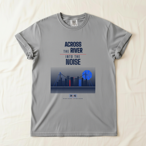 A gray short-sleeve t-shirt laid flat on a light beige fabric background. The shirt features a graphic print on the front with the text 'ACROSS THE RIVER INTO THE NOISE' in navy and red, above a stylized city skyline illustration with blue basketball shaped moon. 