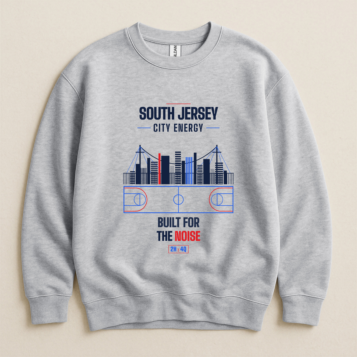 A light gray crewneck sweatshirt with a graphic print on the front featuring a basketball court, a city skyline, and the text 'SOUTH JERSEY CITY ENERGY' and 'BUILT FOR THE NOISE' in navy and red, displayed on a light beige background.