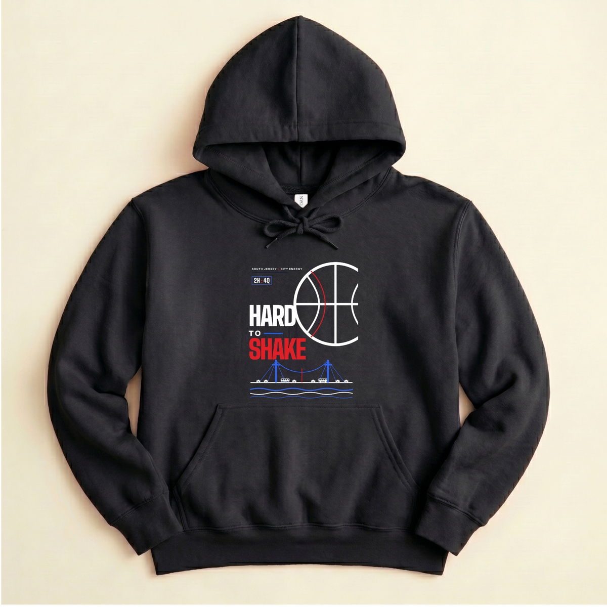 A black pullover hoodie with a graphic print on the front featuring a basketball, the text 'HARD TO SHAKE' in white, red, and a blue suspension bridge illustration, shown against a light beige background.