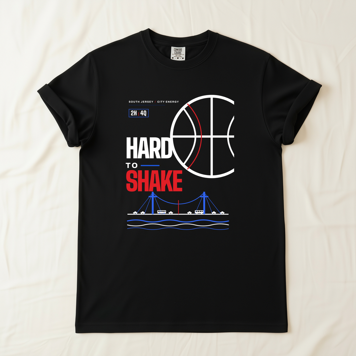 A black short-sleeve t-shirt laid flat on a light beige fabric background. The shirt features a graphic print with a basketball design, the text 'HARD TO SHAKE' in white and red, a small '2H:4Q.