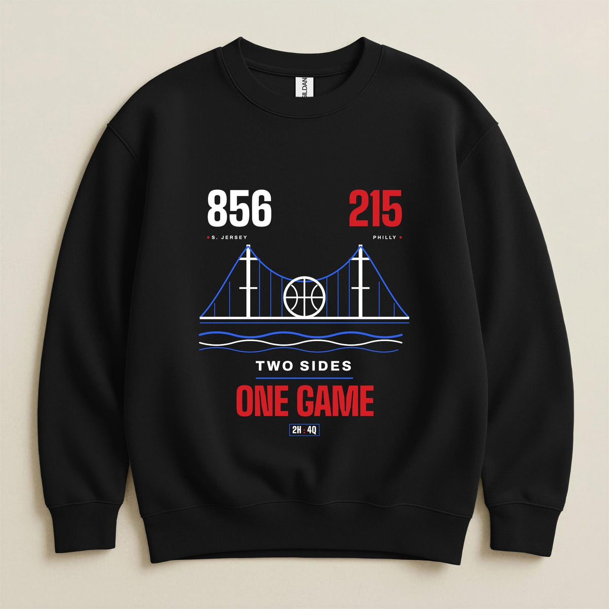 A black crewneck sweatshirt with a graphic print of the South Jersey-Philadelphia connection, featuring the area codes 856 and 215, a bridge design with a basketball, and the text 'TWO SIDES ONE GAME' in white and red on a beige background.