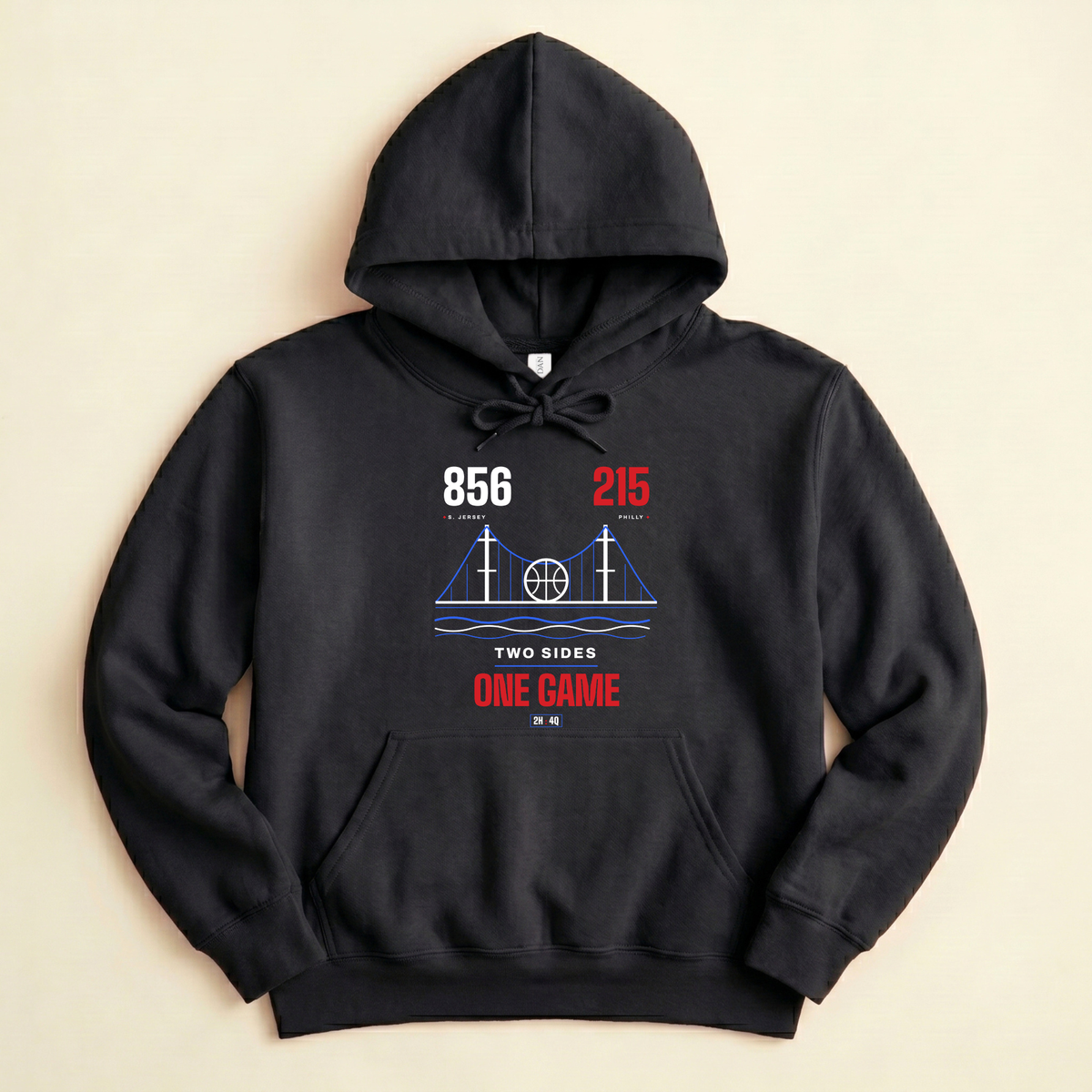A black pullover hoodie laid flat on a light beige background, featuring a vintage-style sports graphic on the chest with the text '856', '215' area codes, and 'TWO SIDES ONE GAME' in red and white.